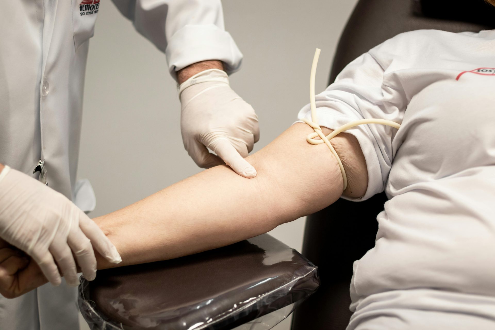 Medizinisches Fachpersonal mit Handschuhen bereitet Patienten mithilfe einer Aderpresse auf die Blutentnahme vor.