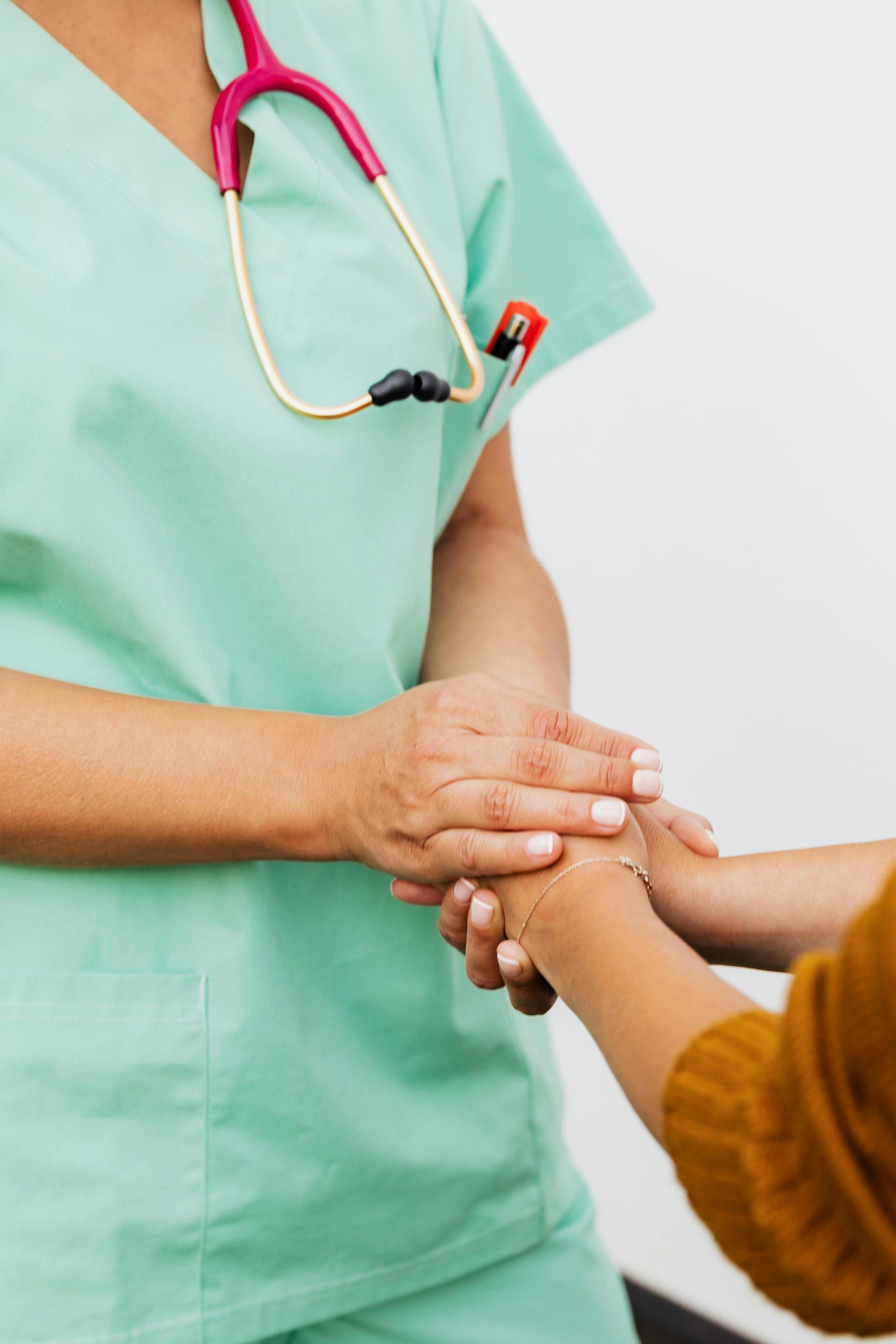 Eine Krankenschwester im grünen Kittel greift sanft nach der Hand eines Patienten und bietet ihm Unterstützung an.