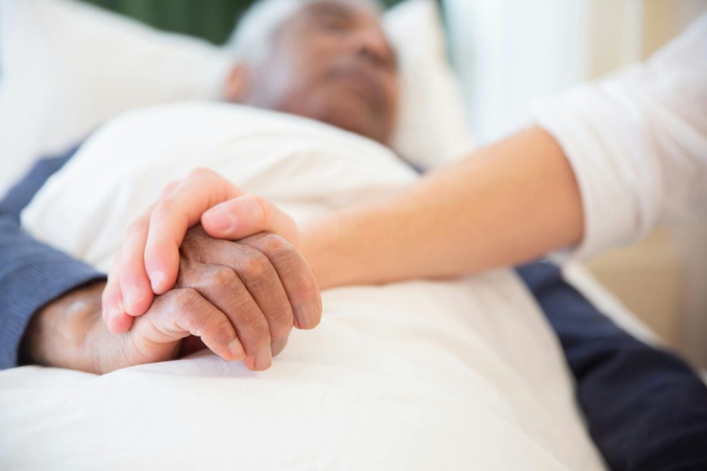 Eine tröstende Geste, wenn im Krankenhaus eine Hand eine andere hält, symbolisiert Fürsorge und Unterstützung.